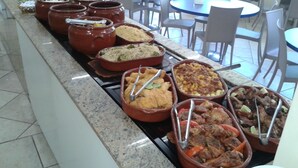 A buffet with various dishes in ceramic containers, arranged on a counter in a dining area with tables and chairs.