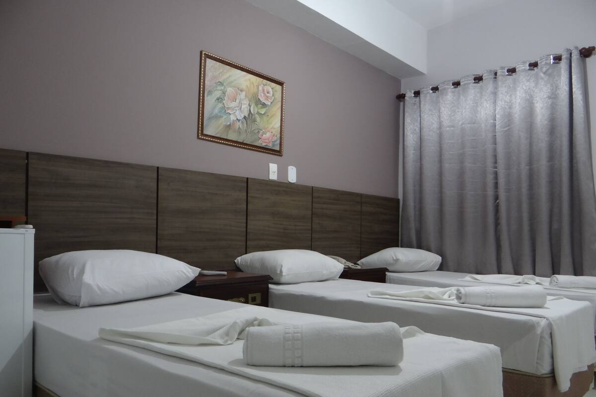 A hotel room with two beds, a wooden headboard, a painting on the wall, and a curtain.