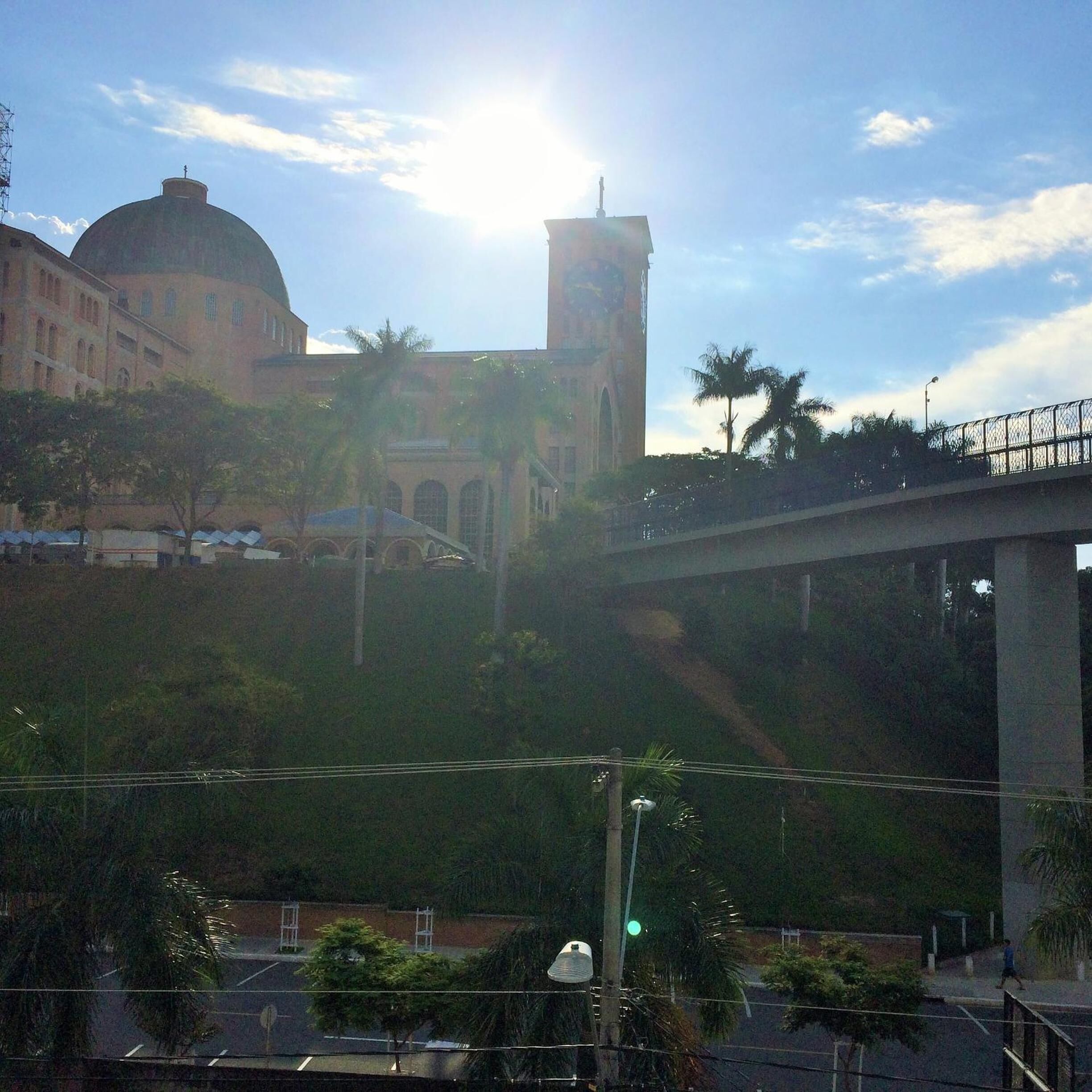 A view of a building with a dome and a tower, a bridge, and palm trees.