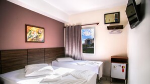 A hotel room with two beds, a painting on the wall, a window with curtains, a TV, and a small refrigerator.