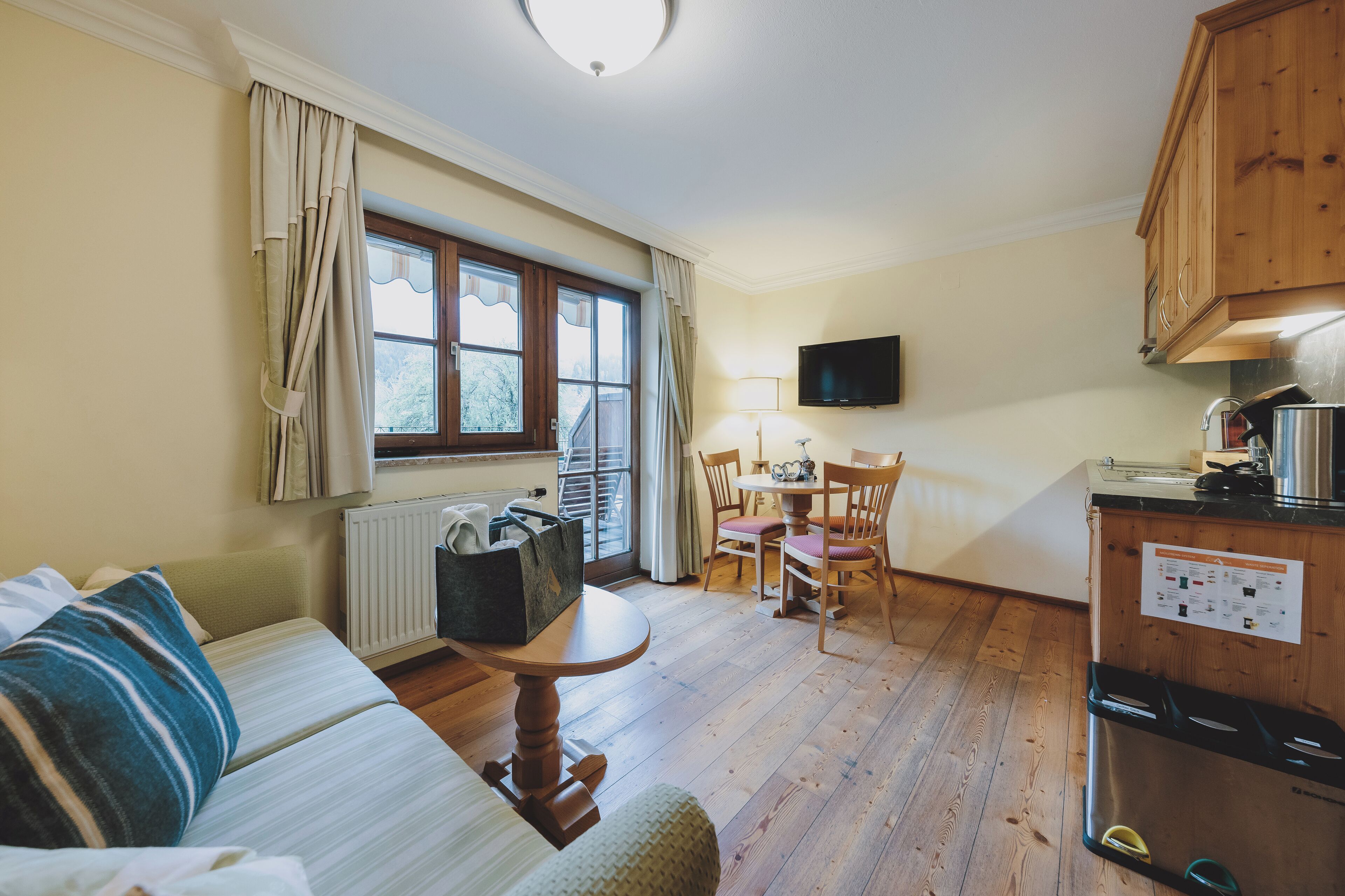 Een gezellige kamer met een bank, een eettafel met stoelen, een aan de muur bevestigde televisie en een houten kast met een kookplaat.