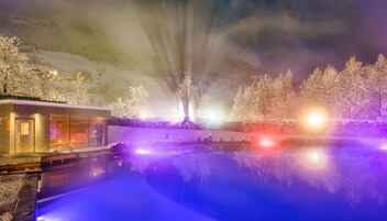 A snow-covered landscape with a reflective pool, a modern building with glass windows, and a mountain in the background.