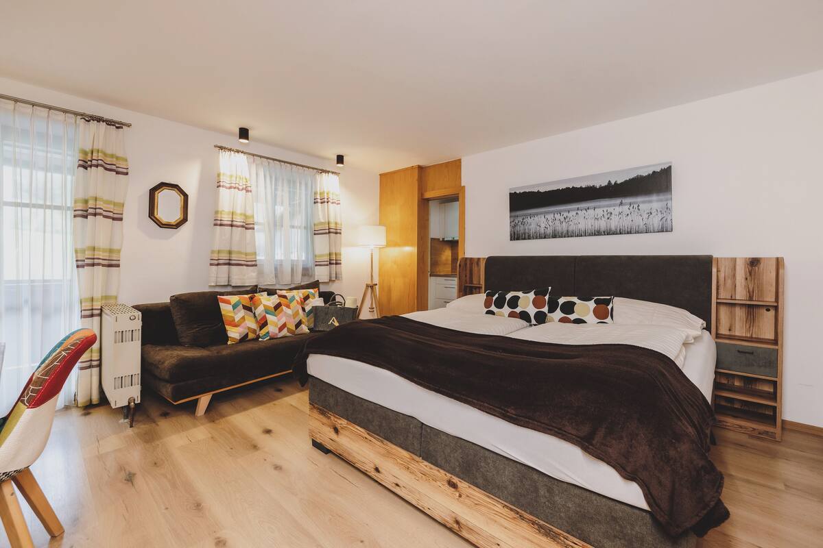 A bedroom with a bed, a sofa, a chair, and a desk.