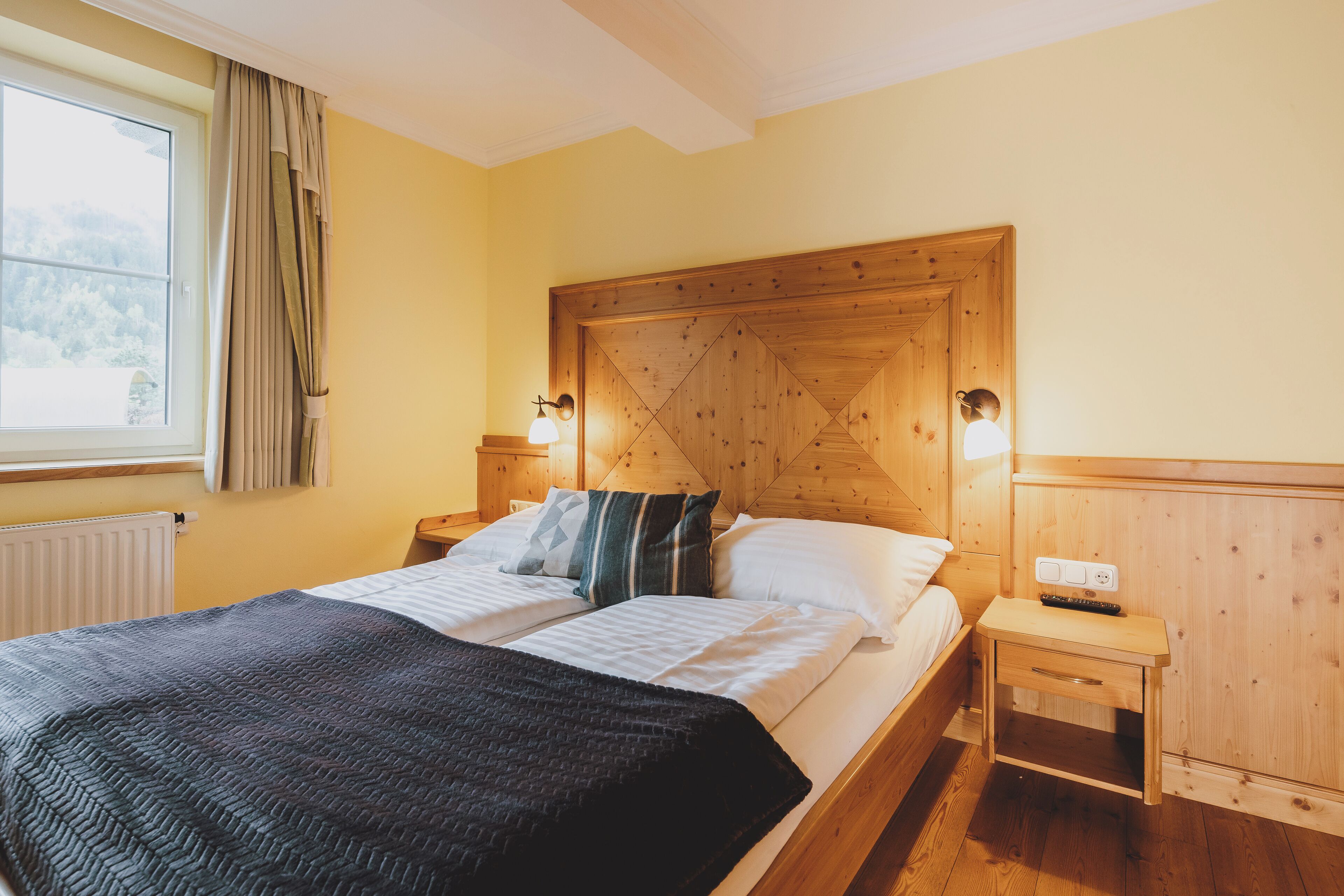 A bedroom with a wooden headboard, two bedside tables with lamps, a bed with white linens, and a window with curtains.