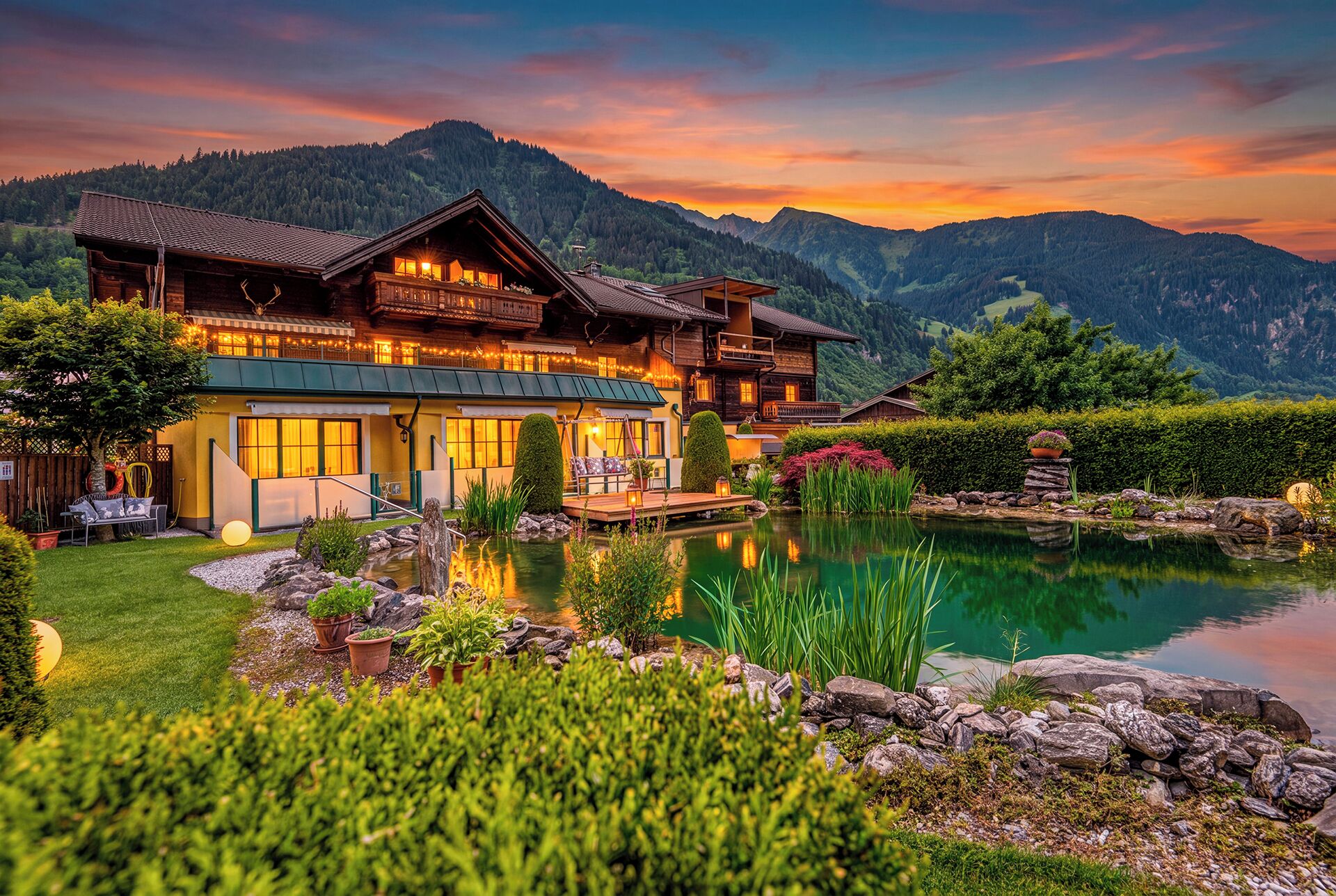 Ein großes Holzhus im Chalet-Stil mit Teich, umgeben von Bergen und üppiger Vegetation.