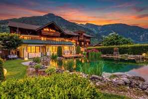 A large wooden chalet with a pond, surrounded by mountains and lush greenery. - Haus Katharina (Bad Hofgastein)