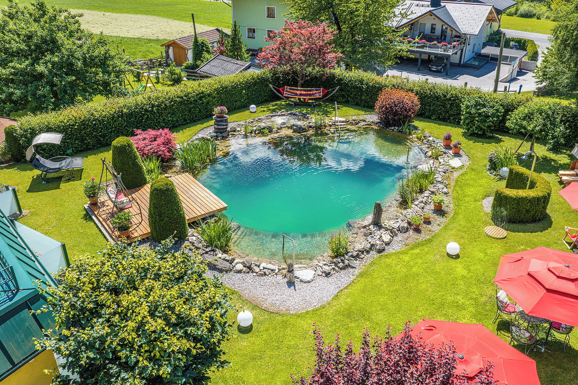 Une piscine circulaire entourée d’une terrasse, elle-même bordée de haies bien entretenues et de diverses plantes.