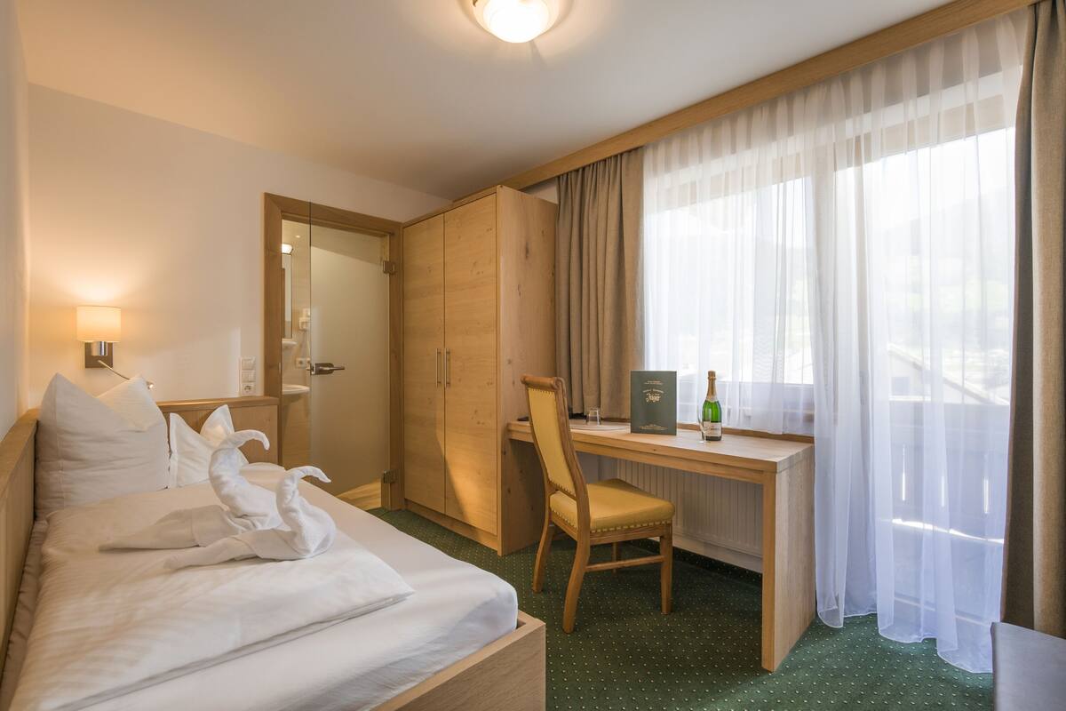 Een hotelkamer met een bed, een bureau, een stoel, een kledingkast en een raam met gordijnen.