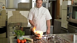 A chef cooking with a flame on a stove in a kitchen with stainless steel appliances and a tiled backsplash. - Hotel - Gasthof Jäger Heim GmbH (Schlitters)