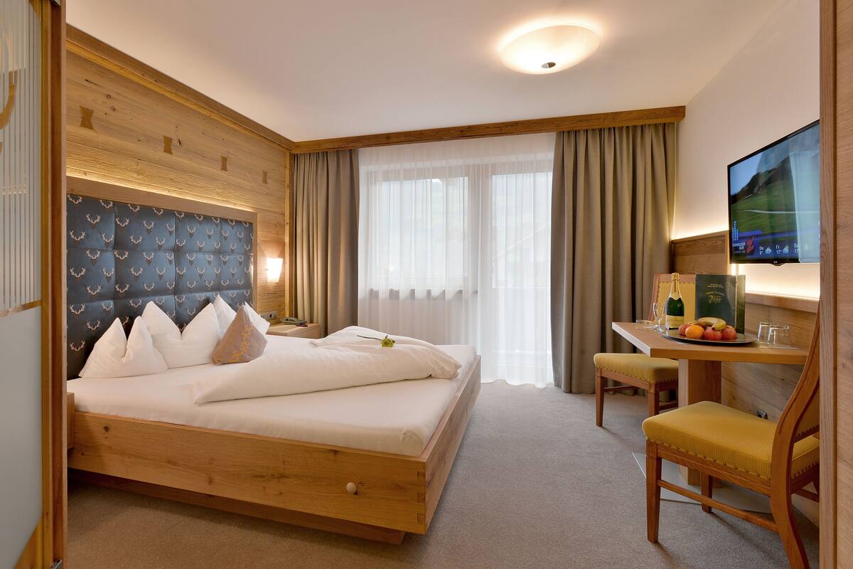 Een hotelkamer met een bed, een bureau met stoel, een televisie en een raam met gordijnen.