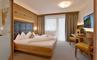 Una habitación de hotel con cama, escritorio con silla, televisor y ventana con cortinas.