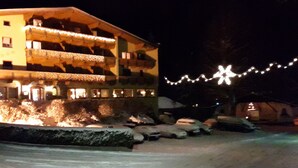 A building with multiple balconies, snow-covered ground, and string lights. - Hotel - Gasthof Jäger Heim GmbH (Schlitters)