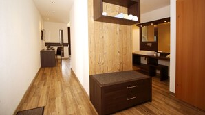 A modern hotel room with a wooden floor, a dark brown dresser, a wooden wall unit with towels, a large mirror, and a wooden door.