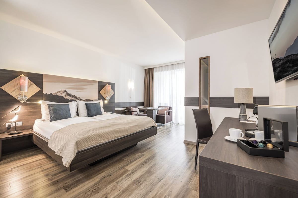 Habitación de hotel moderna con una cama grande, un escritorio con computadora, televisor y ventana con cortinas.