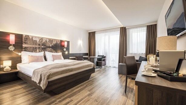 A hotel room with a large bed, a desk with a computer, a chair, and a TV.