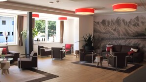 A modern living room with a large window, a mountain mural, and a red accent wall.