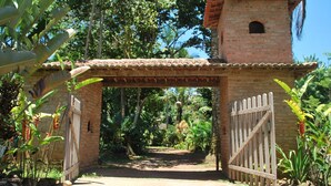 Uma construção de tijolos com telhado de cerâmica, um portão de madeira e um caminho que serpenteia por um jardim exuberante.