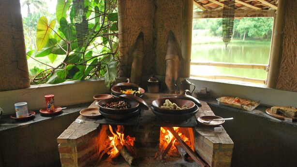 Uma lareira de tijolos com panelas e frigideiras, cercada por janelas com vista para vegetação e água.