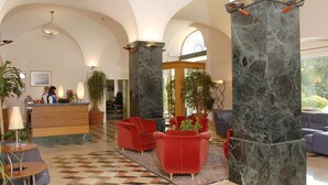 A lobby with a check-in desk, red armchairs, a checkered floor, and marble pillars. - Hotel Vecchio Mulino (Monopoli)