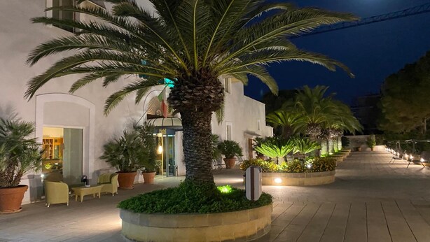 A hotel courtyard at night with palm trees, outdoor seating, and a moon in the sky. - Hotel Vecchio Mulino (Monopoli)