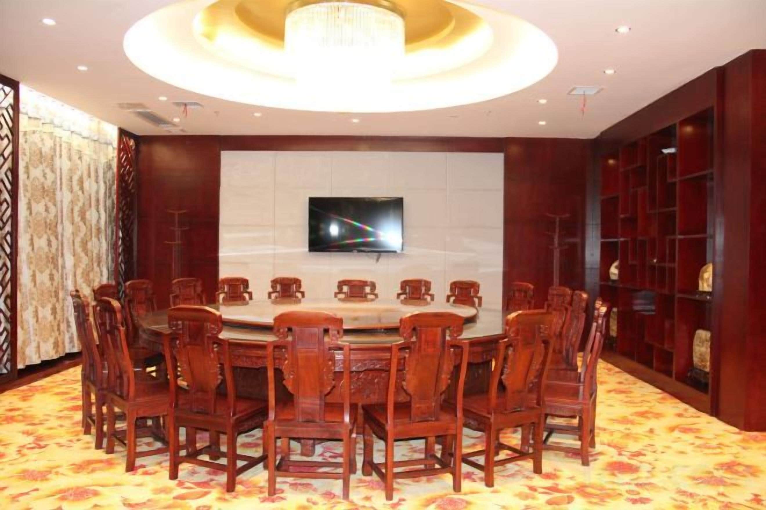 A conference room with a round table, chairs, a television, and a patterned carpet.
