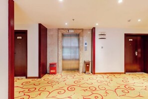 A hotel lobby with a carpeted floor, an elevator, and a trash bin. - Zhongmei Hotel (Jinggangshan)