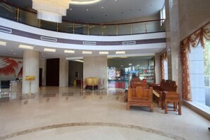 Um hall espaçoso com teto alto, área de estar com móveis de madeira e vista para uma loja ao fundo.