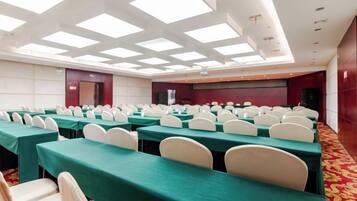 Un salón de conferencias con filas de mesas y sillas, un escenario y un techo alto con tragaluces.