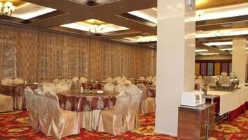 Un salón de banquetes con mesas redondas, sillas y una zona de buffet.