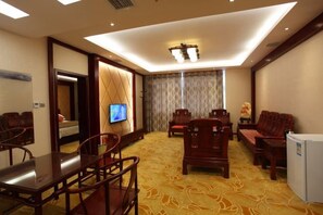 A hotel room with a large bed, a television, a dining table with chairs, and a small refrigerator. - Zhongmei Hotel (Jinggangshan)