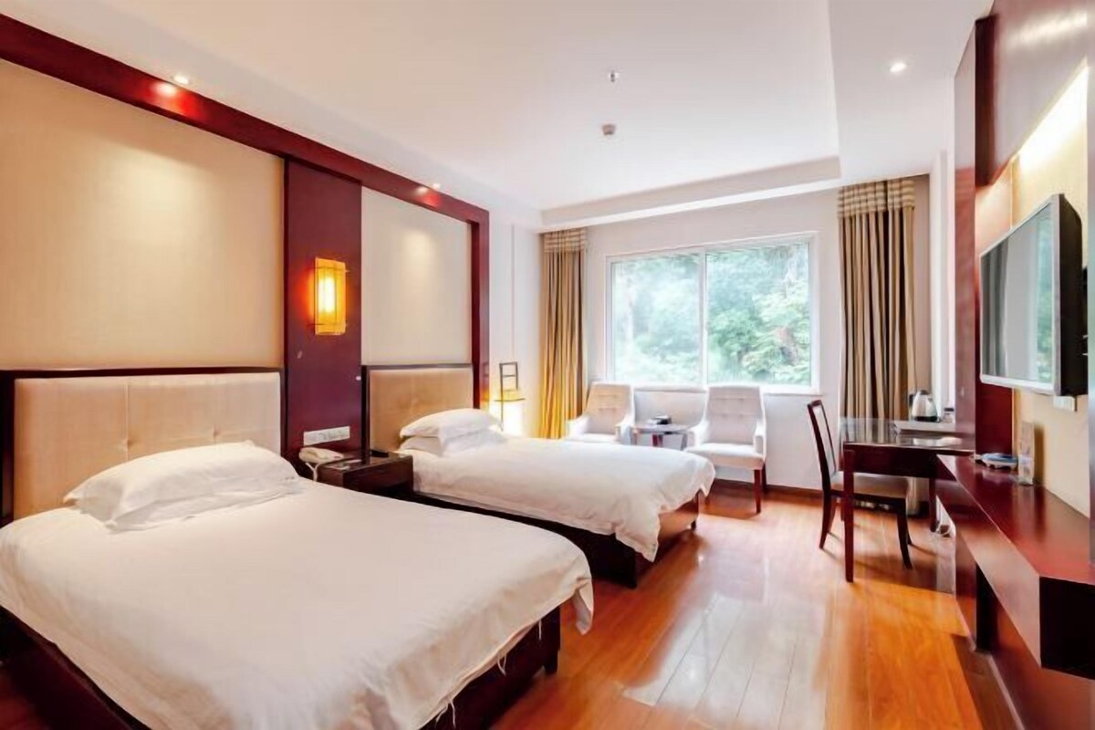 A hotel room with two beds, a desk, a chair, and a TV.
