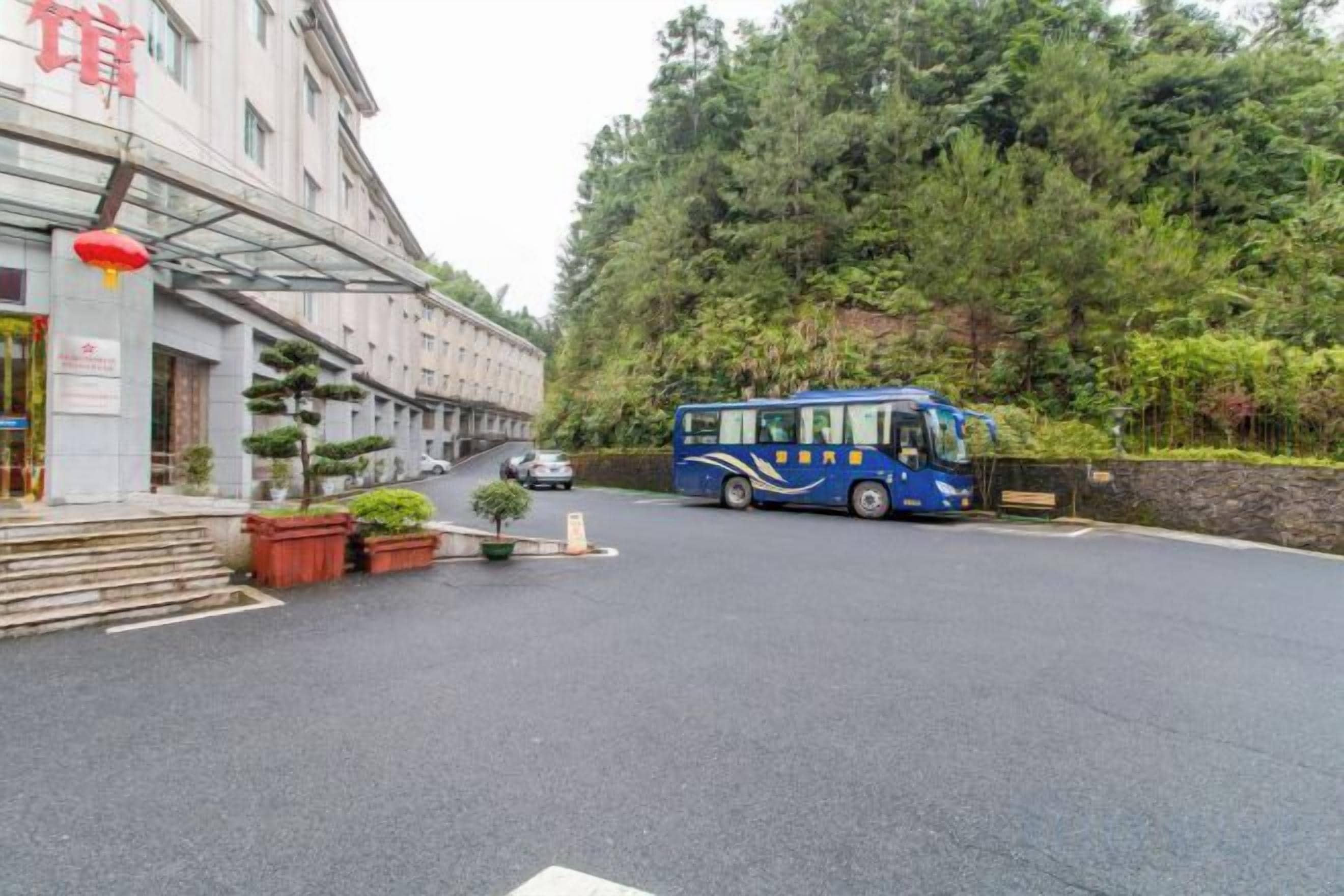 A building with a bus parked in front, surrounded by trees and a paved area.