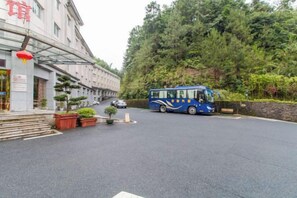 A building with a bus parked in front, surrounded by trees and a paved area. - Zhongmei Hotel (Jinggangshan)