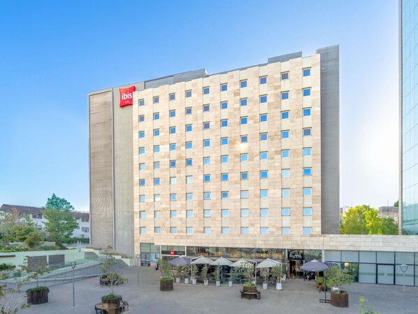 A hotel with a modern facade, multiple floors, and a courtyard with outdoor seating. - ibis Santiago Las Condes (Santiago)
