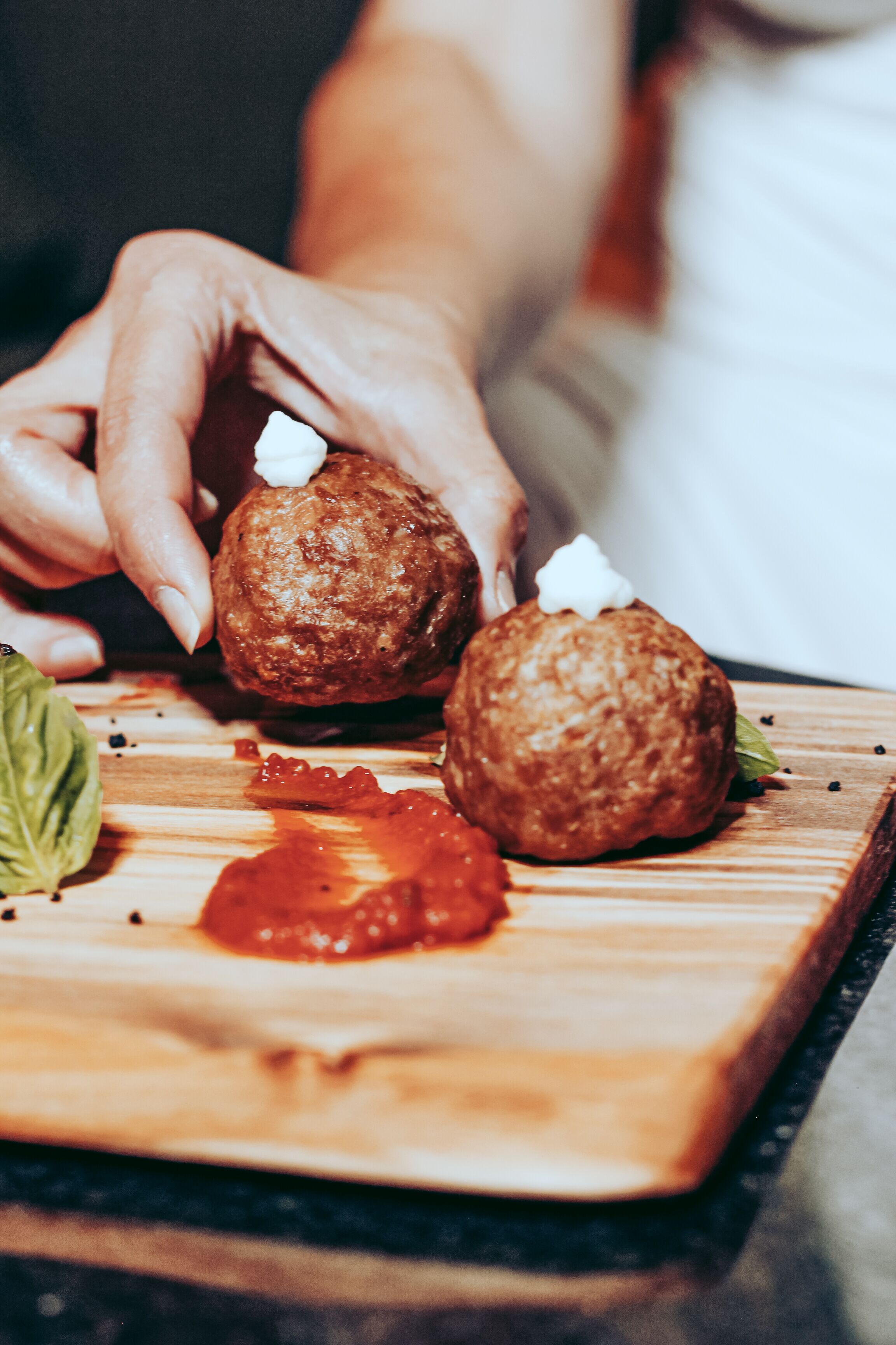 A wooden cutting board with two meatballs and a dollop of sauce.