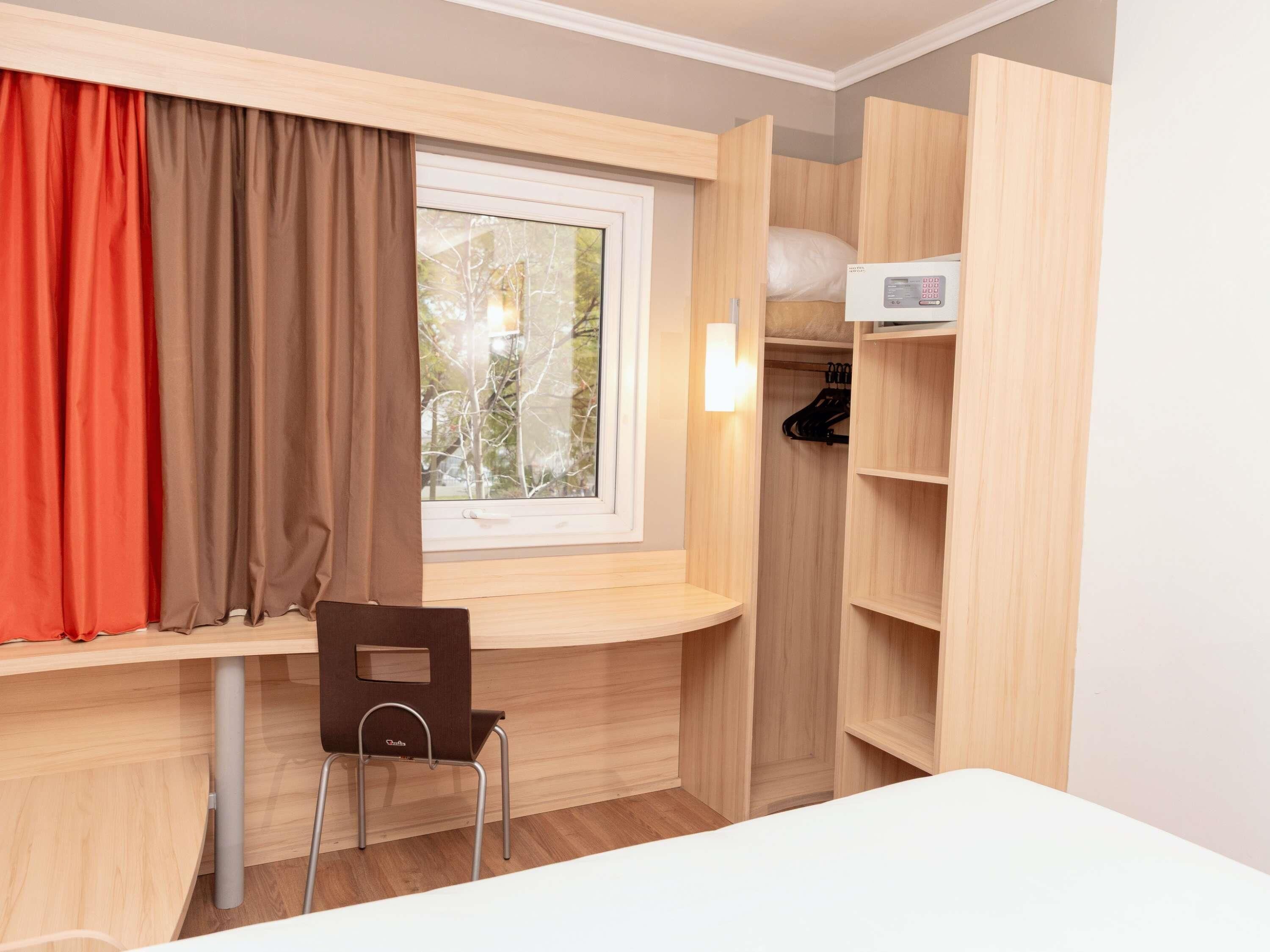 Habitación pequeña con ventana, escritorio, silla y armario.