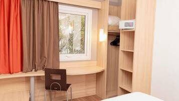 Habitación pequeña con ventana, escritorio, silla y armario.