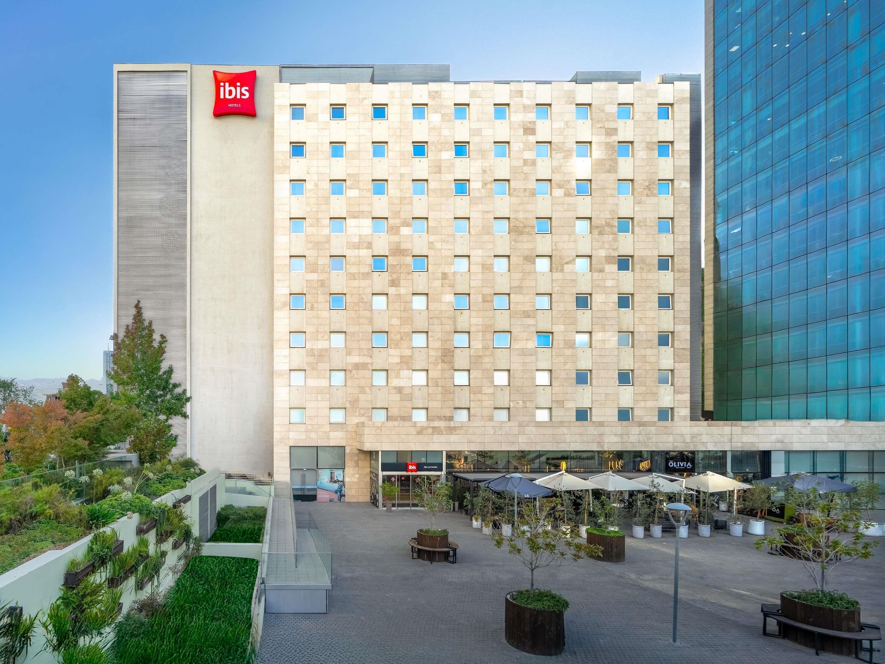 Un hotel moderno con una fachada de ventanas enrejada, asientos al aire libre y un jardín en la azotea.