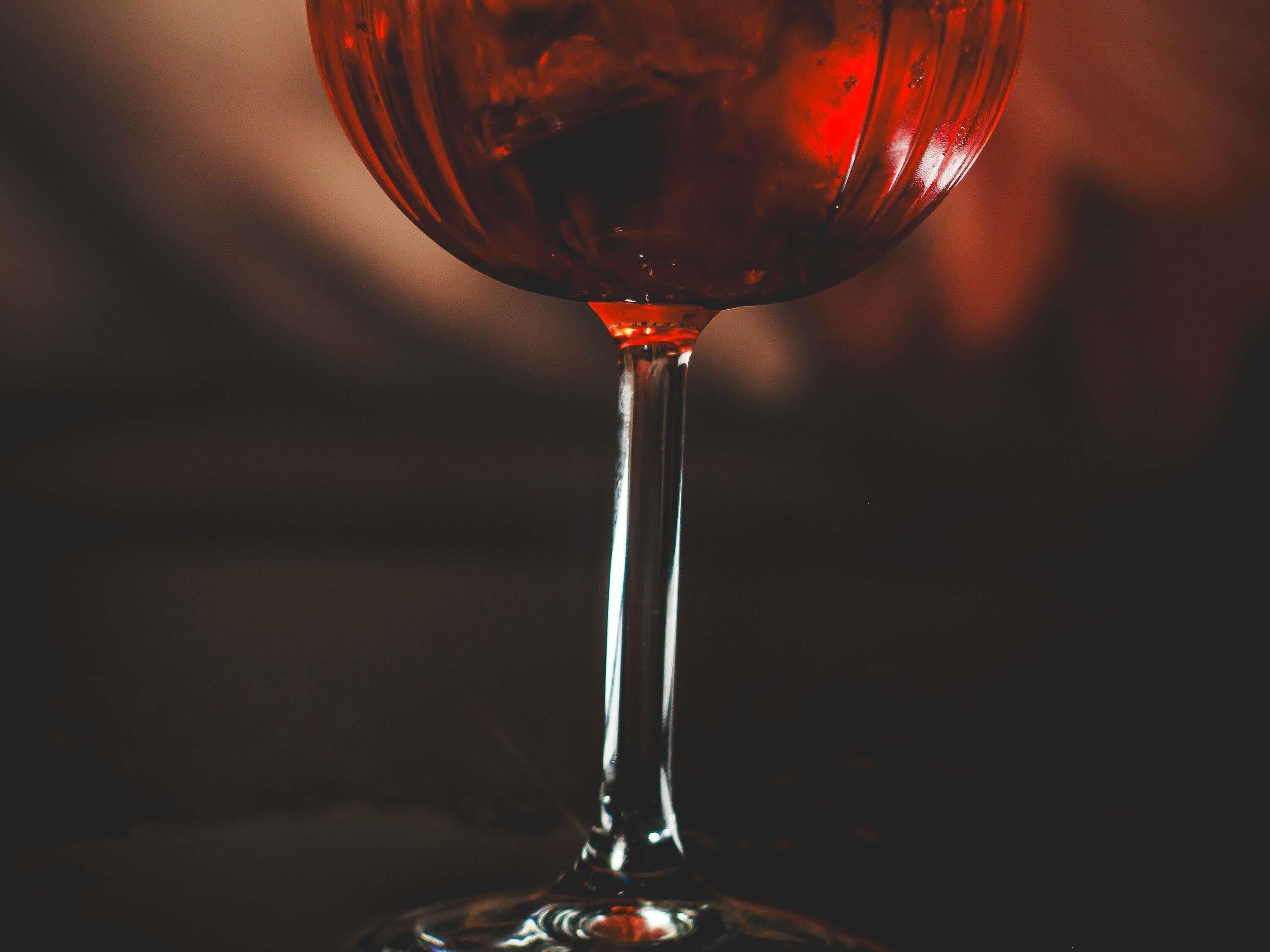 A close-up of a wine glass with a dark liquid, possibly red wine, on a reflective surface.