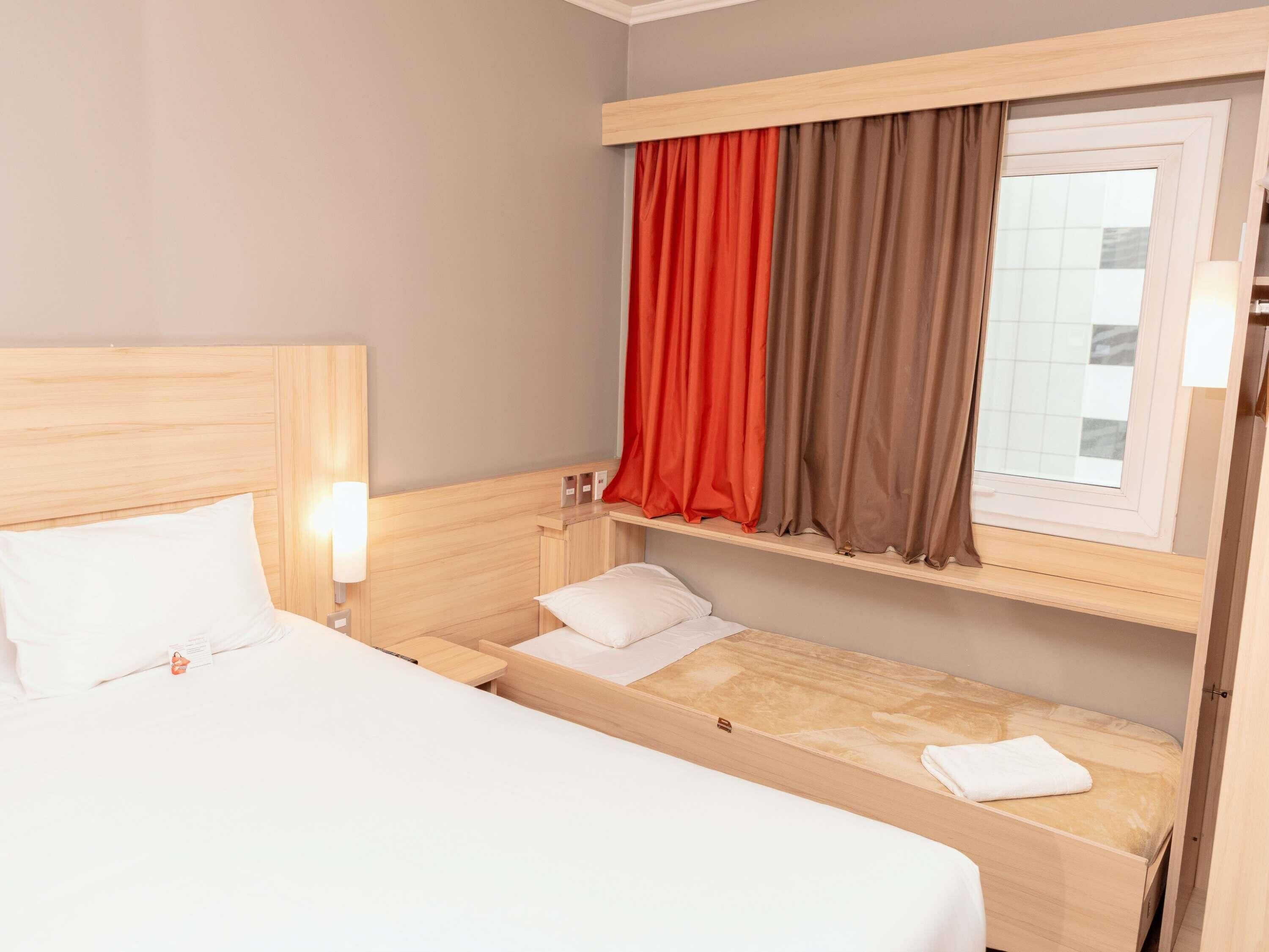 Hotellihuone, jossa on yksi sänky, yöpöytä, pieni työpöytä ja ikkuna, jossa on verhot.