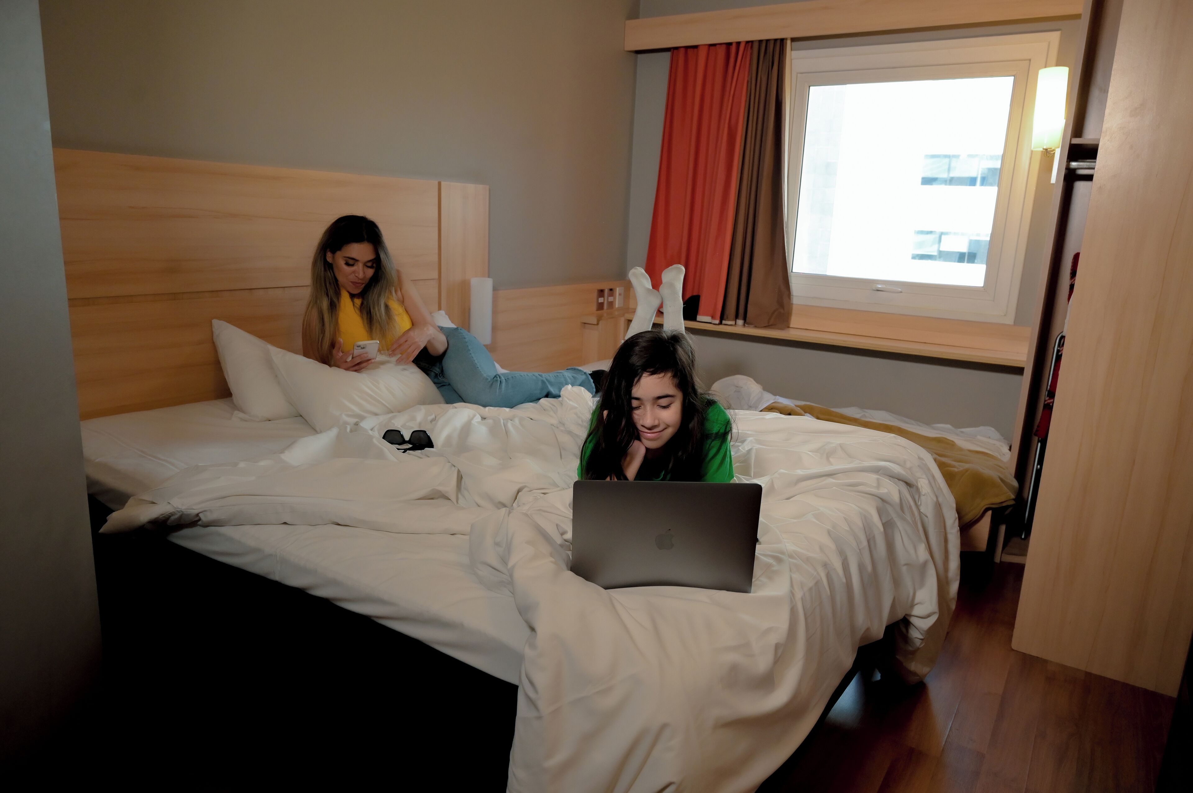 A hotel room with a bed, a window with curtains, and a wooden headboard.