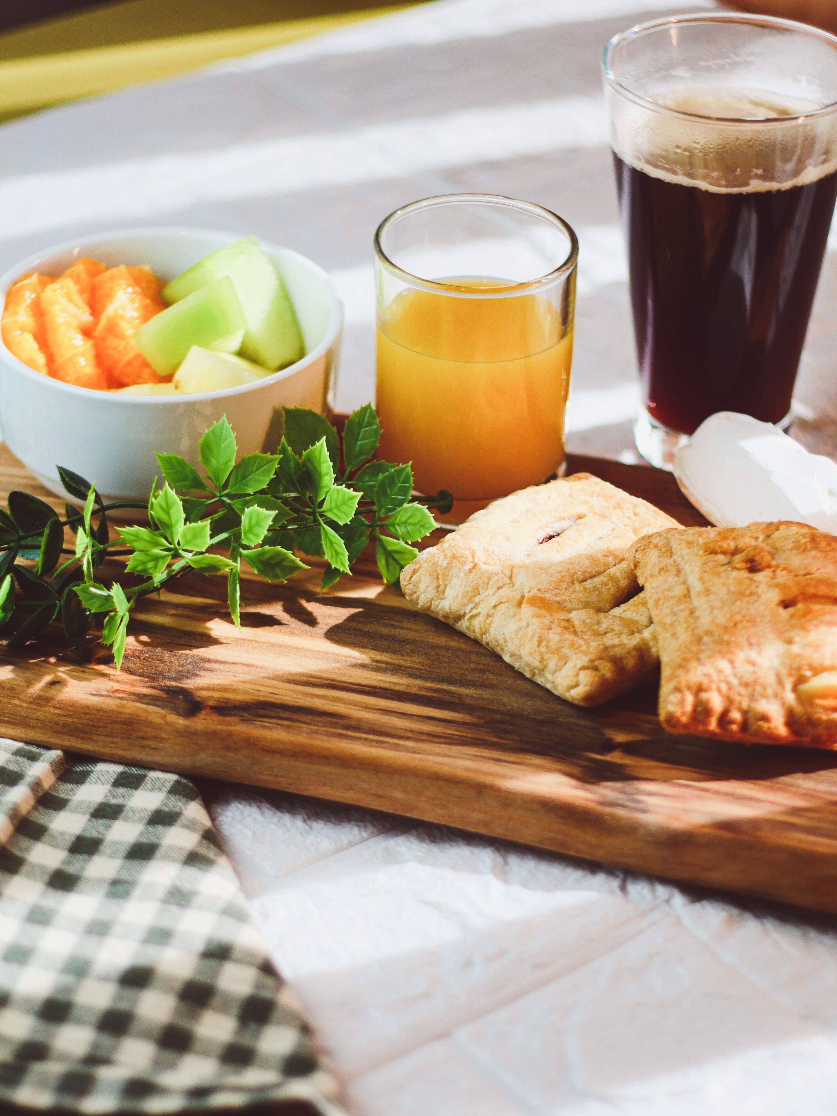 A wooden board with food items, a glass of orange juice, and a glass of dark beverage.