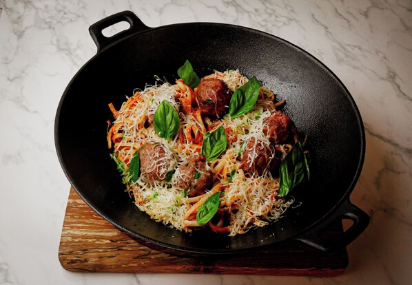A skillet with meatballs, spaghetti, and cheese on a wooden board.