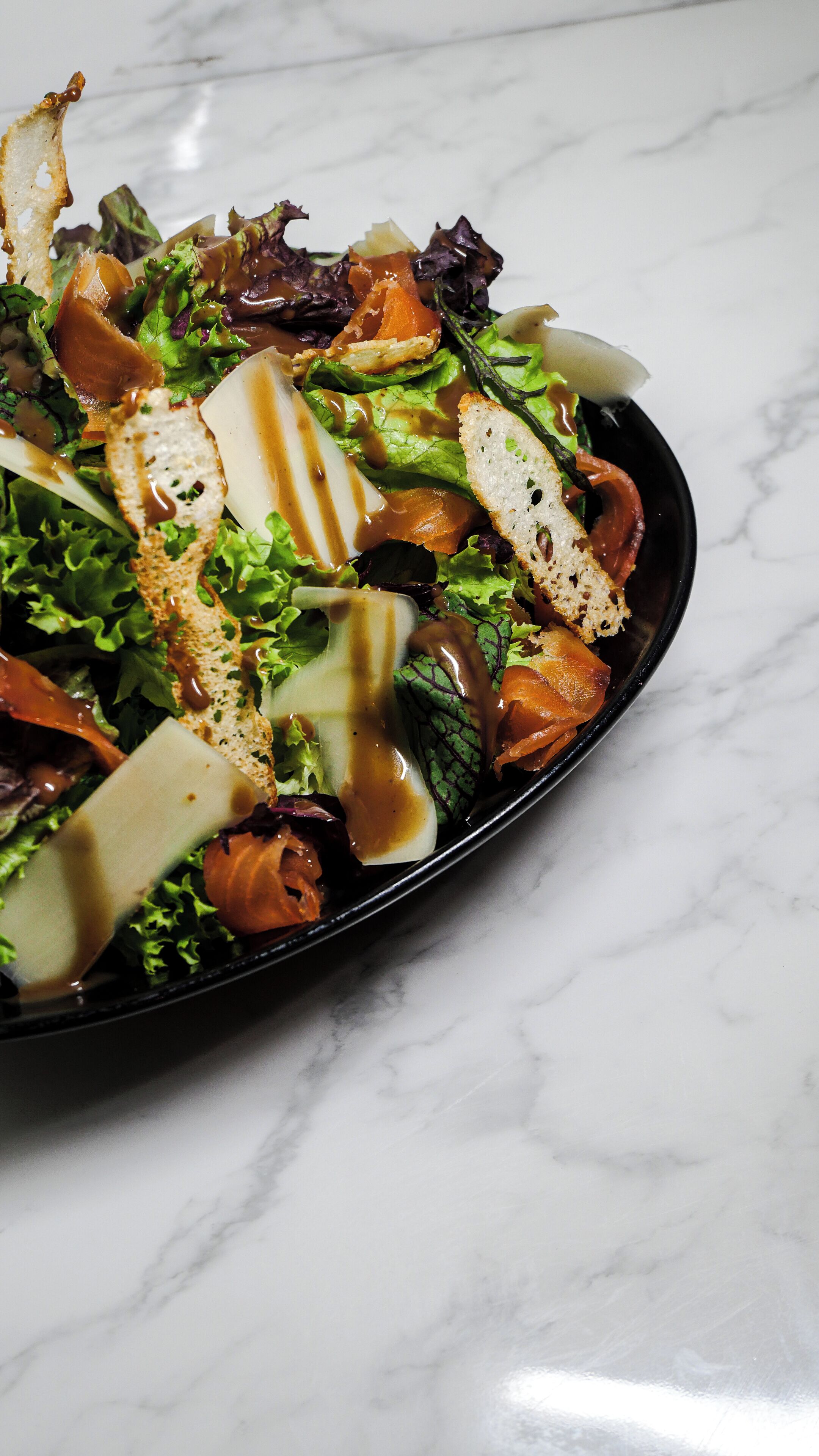 A salad with various ingredients and a dressing, served on a black plate.