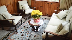 Een kamer met houten lambrisering, twee witte fauteuils, een houten bijzettafeltje met een bloemstuk en een kamerbreed tapijt met een patroon.