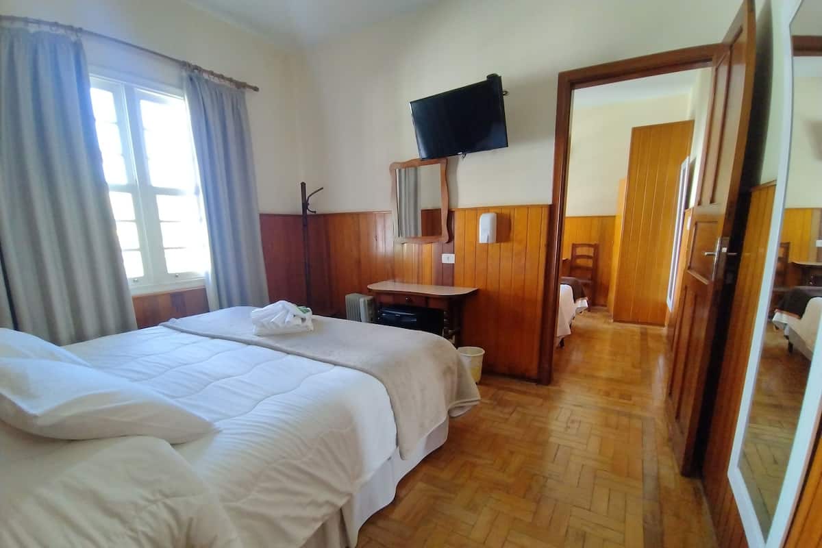 Habitación de hotel con dos camas, televisión, escritorio y baño visible a través de una puerta abierta.