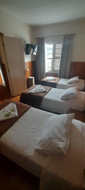 Une chambre d’hôtel avec deux lits, un téléviseur fixé au mur et une fenêtre avec des rideaux.
