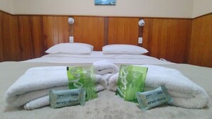 Een hotelkamer met een houten hoofdeinde, twee witte kussens en een zacht wit tapijt. Er liggen twee pakketjes met de tekst 'erva-doce' op het tapijt.