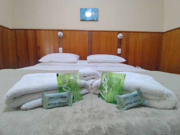 A hotel room with a wooden headboard, two white pillows, and a fluffy white carpet. There are two packages labeled 'erva-doce' on the carpet.