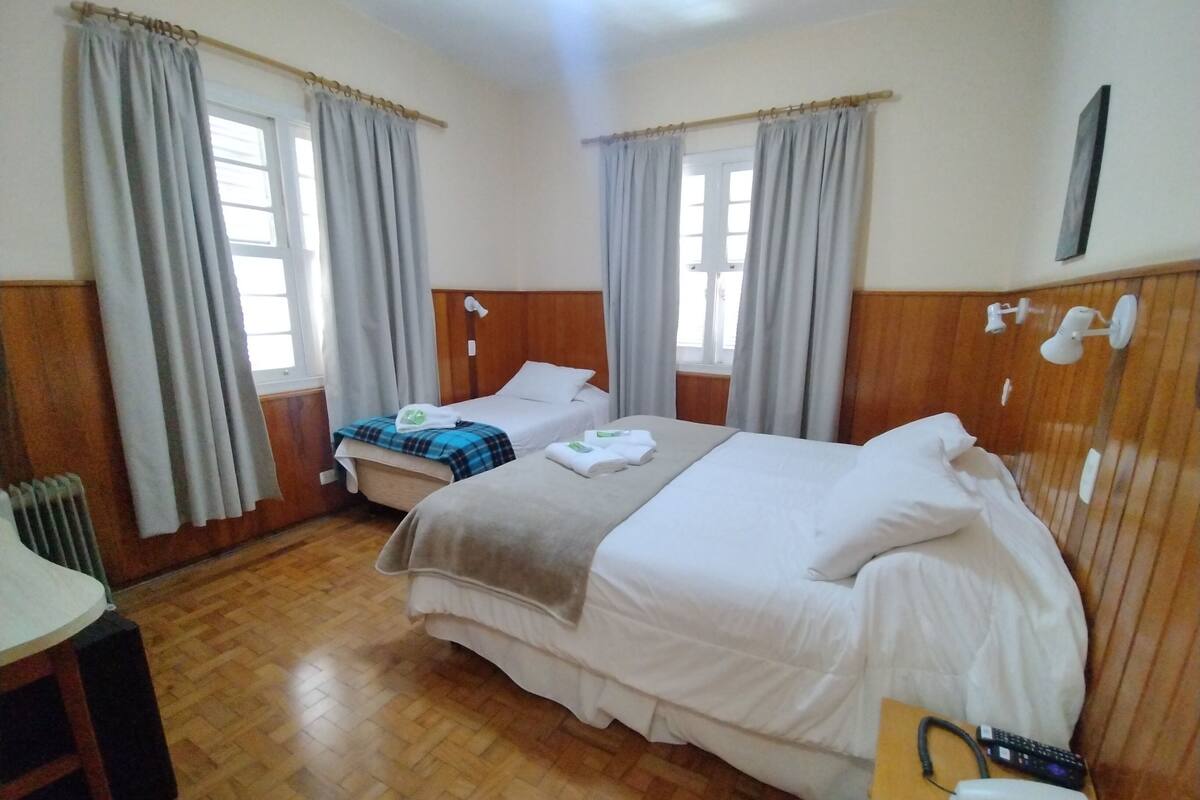 Una habitación de hotel con dos camas, piso de madera, escritorio con teléfono y radiador.
